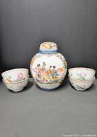 Full lot photo showing the covered ginger jar centered with four handleless cups arranged around it, all with colorful Famille Rose overglaze enamel decoration on white porcelain.