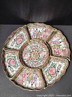 Top view of entire set showing central round dish surrounded by six matching dishes with scalloped edges, intricate hand painted people, flowers, and butterflies.