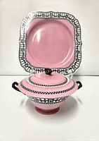 Large pink lidded pot with black handles and decorative black and white pattern with square pink plate behind