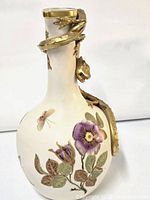 Front view of white porcelain ewer showing multicolor enamel floral and insect motifs with gilt dragon handle.