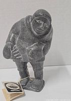 Front view of the soapstone carving showing detailed carving of the figure’s face and clothing with attached original paperwork tag.