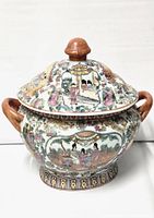 Front view of the small antique famille rose tureen with lid, showing detailed painted scenes of figures, flowers, and birds in pale pink and other colors. Two side handles and wooden-like knob on lid visible.