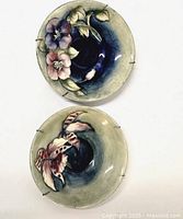 Top view of two Moorcroft floral pottery wall plates with different flower designs and metal hangers.