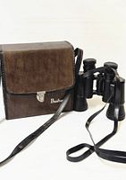 Photo showing vintage Bushnell binoculars standing upright alongside original brown leather carrying case with shoulder strap and front clasp