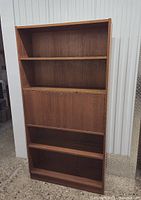 Front view of the vintage veneer bookcase showing four fixed shelves and the closed middle drop-down shelf area.