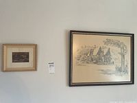 Two framed art pieces hanging on the wall, a larger black framed sketch by Robert G. Kemp on the right and a smaller gold-toned framed needlepoint on the left