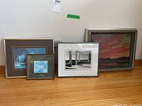 Four framed art pieces including two prints with mats, one black and white photo print, and one large oil painting with ornate frame.