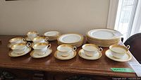 Full view of 8 teacups and saucers alongside stacked dinner, dessert, and bread & butter plates on wooden table.