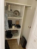Wide shot of pantry shelf showing assortment of bakeware including metal pans, glass bowls, and measuring cup