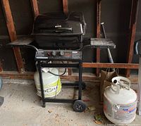 Front view of the black Master Chef BBQ grill on cart with two propane tanks on floor next to it.