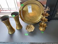 Photo showing the full lot on table: two brass vases, large brass tray, small trinket dish, and three-tiered brass diya with bird figure on top.