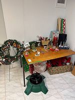 Wreath and various Christmas decorations displayed on table and floor including lantern, musical tree, ornaments, and gift wrapping supplies.