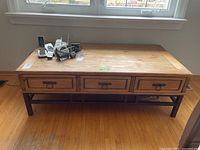 Front view of wooden coffee table showing three drawers with metal handles and wood top surface with some items on it.