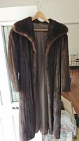 Full length front view of dark brown 3/4 length fur coat hanging on wood hanger.
