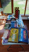 Full table view with all games and accessories including Monopoly, Clue, Scrabble, Mystery Mansion, puzzles, checkers, chess, and game supplies.