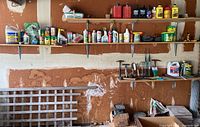 Garage wall shelf with garden chemicals and automotive supplies such as fertilizers, pest repellents, motor oil bottles, plastic Jerry cans, and garden sprinklers
