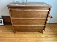 Front view of the dresser showing three drawers and wood grain finish with some wear marks.