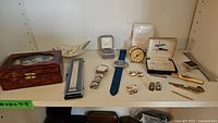 Photo of assorted wristwatches, cufflinks, tie clips, watch bands, a decorative wooden box and a black and white ceramic dish.