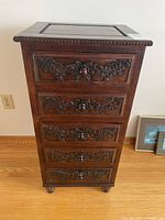 Front view of the wooden dresser showing five drawers with carved floral details and wooden knobs.