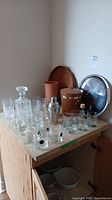 Full view of barware set on a wooden surface including glassware, decanter, cocktail shaker, two trays, wine cooler, and ice bucket.