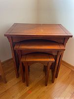 Set of three wooden nesting tables stacked together to show size progression and design.