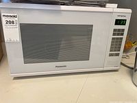 Front view of white Panasonic microwave showing door, window with ventilation slats, keypad and digital display with timer.