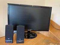 Front view of Samsung monitor with two black Cyber Acoustic speakers placed in front. Monitor has cables coiled on its base.