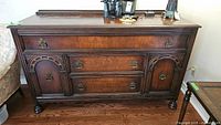 Front view of antique wooden sideboard showing carved details and brass hardware.