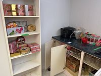 Shelf with assorted vintage tins in floral and striped designs, a round tin with birds and flowers, and a large black enamel pot with lid on countertop beside red paraffin wax packs and a metal potato masher
