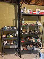 Black metal shelving units with assorted household tools, light bulbs, caulk tubes, hammers, electrical tapes, open solvent containers, light fixture.