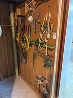 View of assorted hand tools hanging on a wooden wall and pegboard, including extension cords, clamps, wrenches, and screwdrivers.