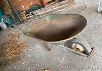 Side angle view of green metal wheelbarrow showing rust and solid rubber tire.