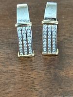Front view of both earrings upright showing three rows of pavé-set stones and yellow gold accents