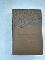 Front cover of the brown hardcover book with embossed illustration and title 'Uncle Tom's Cabin' by Harriet Beecher Stowe.