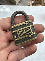 Front view of the small vintage Guard padlock showing the embossed 'GUARD' text with black and brass metal body.