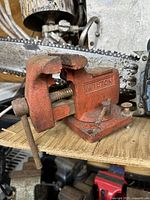 Side view of the orange cast iron Wilton vise showing the vise jaws and tightening screw handle with rust spots.