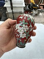 Front and side views of a small Japanese cloisonné vase with floral decoration and noticeable damage on one side.
