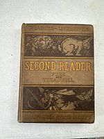 Front cover of the antique textbook showing the title 'Second Reader' with embossed artwork and gold text.
