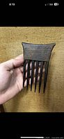Front view of antique ebony wood hair comb showing six prongs and carved geometric patterns on the upper rectangular portion.