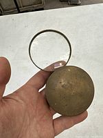 Magnifying glass held in hand with cover detached, showing size and brass finish.