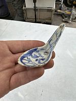 Hand holding antique Chinese blue and white porcelain spoon showing overall shape and handle design.