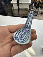 Handheld photo of the antique porcelain spoon showing front design with blue dots and central leaf pattern.