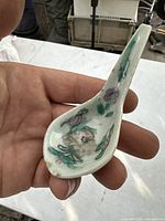 Porcelain spoon showing hand-painted floral design on the inside bowl and handle with signs of age and residues.