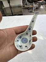 Full view of the porcelain spoon held in hand showing overall shape and decoration.