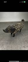 Front view of black wooden pig sculpture adorned with antique coins on body and woven cord design, showing overall form and condition.
