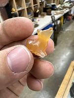 Close-up photo of small translucent amber-colored stone deer/calf figurine held between thumb and index finger showing the left side and front.