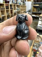 Front view of a small carved dog figurine held between fingers, showing facial details and front legs.