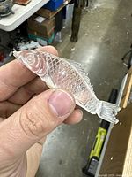 Close-up of the translucent stone fish netsuke held between fingers, showing detailed scales and face features.