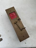 Top view of antique brass emergency break glass box showing red break glass with visible crack and attached hammer on a chain.