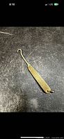 Goldtone folding lace tool laid flat on surface showing entire length and hook end.
